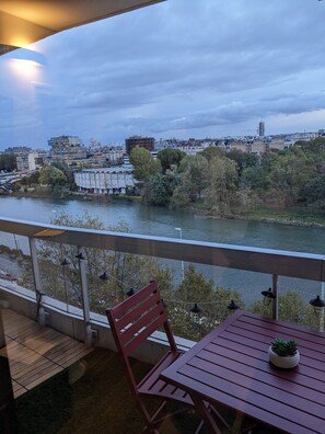 Enjoy the serene river and city views from this balcony, featuring a table and chair.