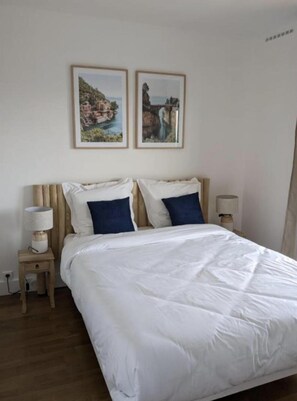 Relax in a serene space with a comfortable bed, bedside lamps, and coastal views.