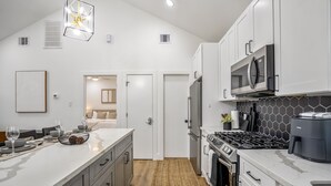 A modern kitchen with white cabinetry, a large island, a stove, and a microwave. - Nestled Nook Bungalow #7033A (Houston)