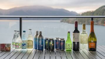 A variety of beverages on a wooden table with a scenic lake and mountains in the background.