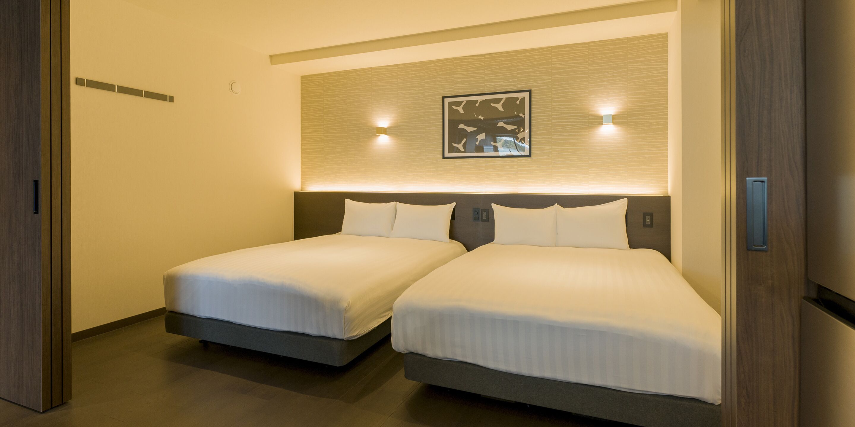 A hotel room with two beds, a wall-mounted artwork, and a ceiling light.