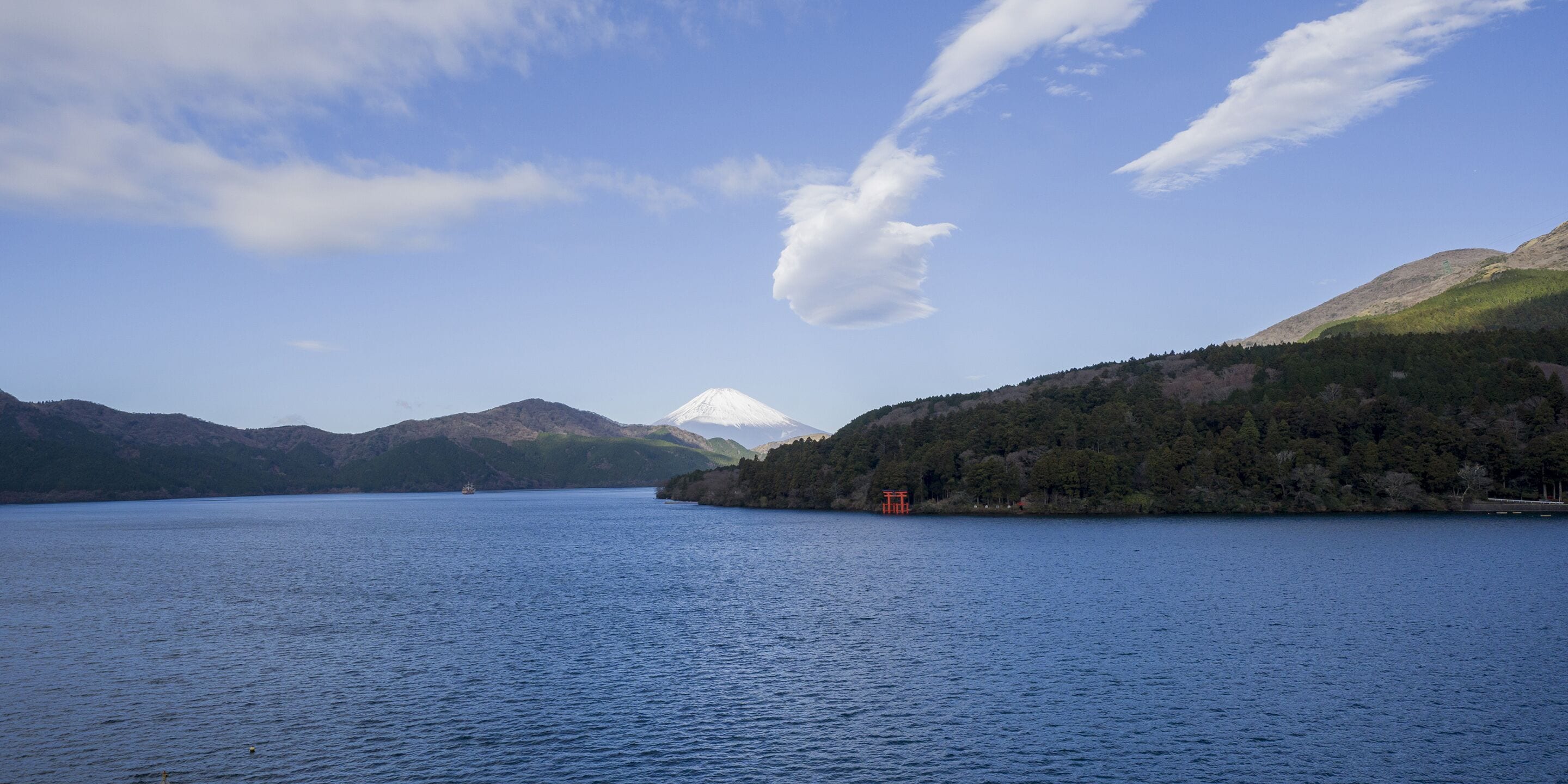 A calm lake with mountains in the background and a small red structure on the right.