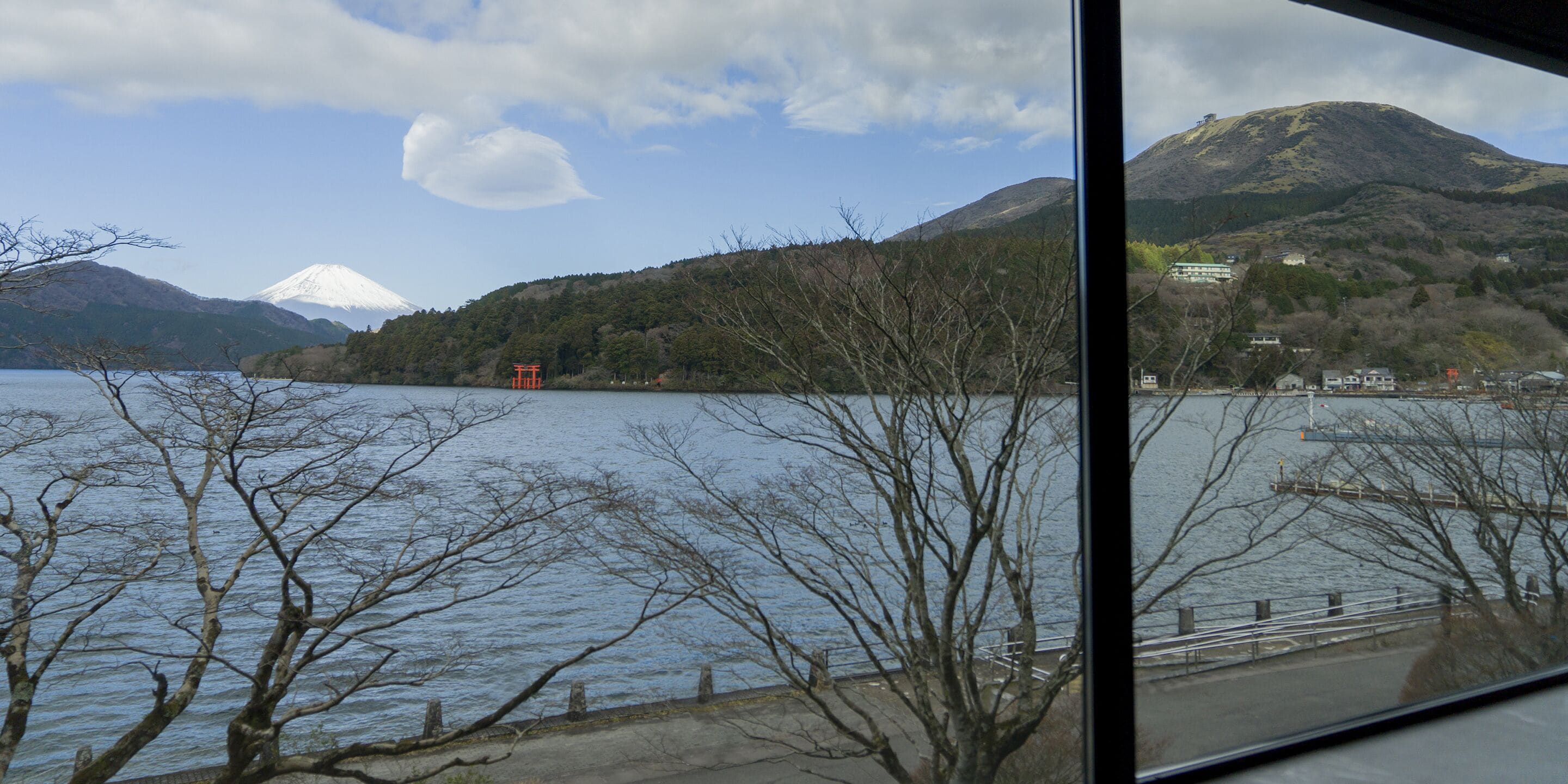 A view of a lake with mountains in the background, a bridge, and some buildings.