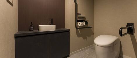A modern bathroom with a dark countertop, a white sink, a toilet, and a towel dispenser.