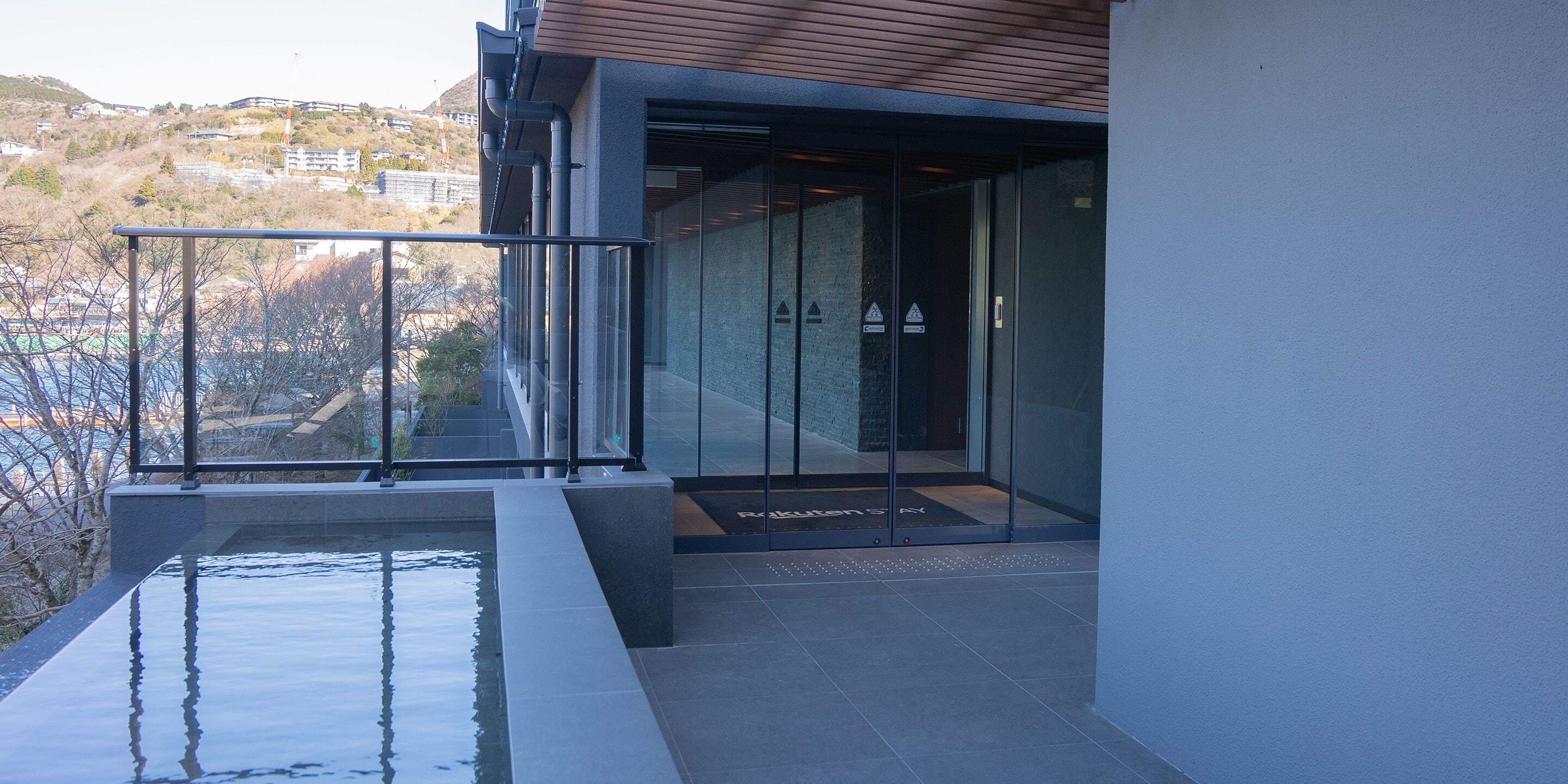 A modern building with a glass entrance, a small outdoor pool, and a view of a hilly landscape.