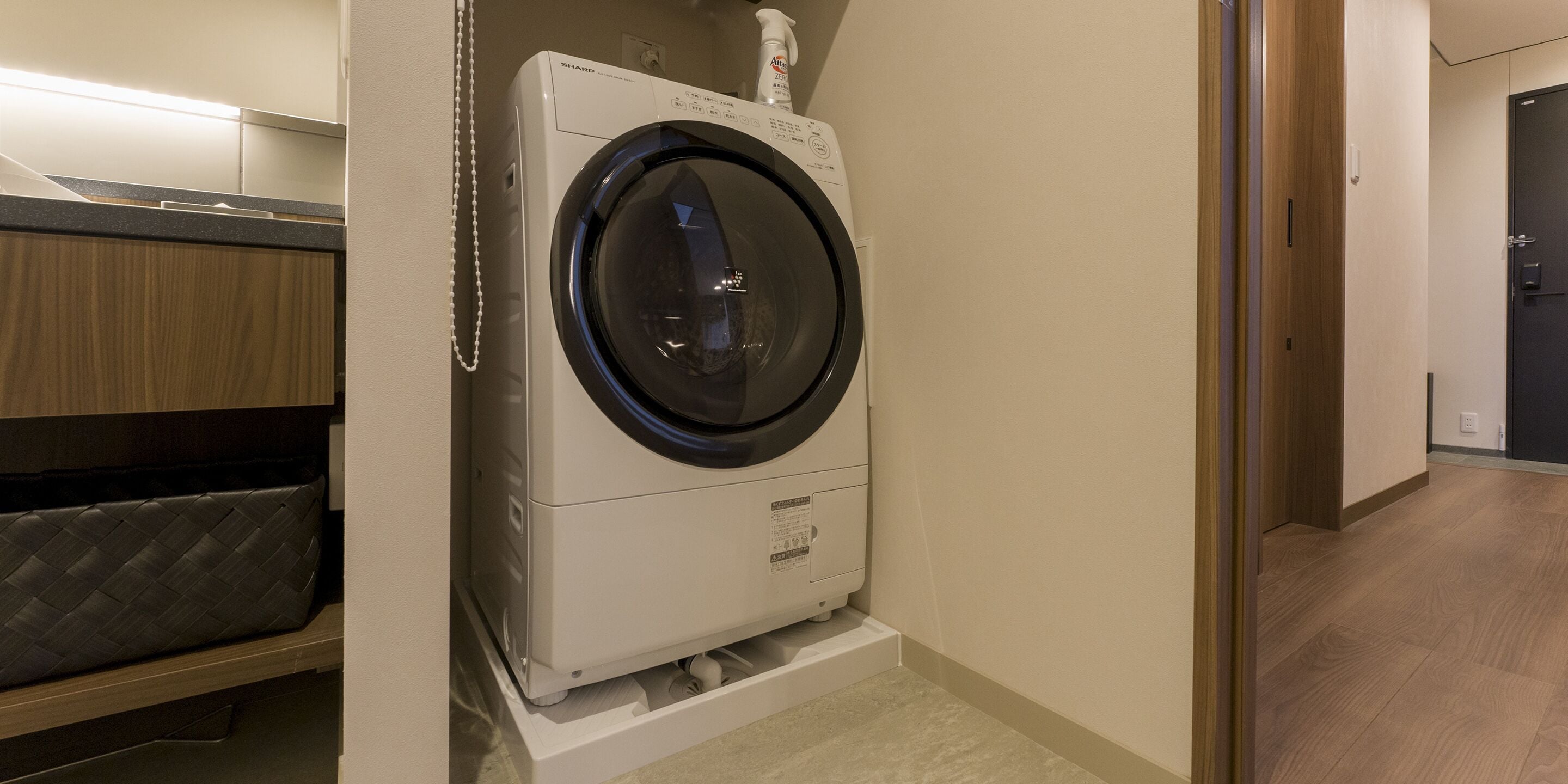 A compact, modern laundry room with a front-loading washing machine, a wooden cabinet, and a small shelf.