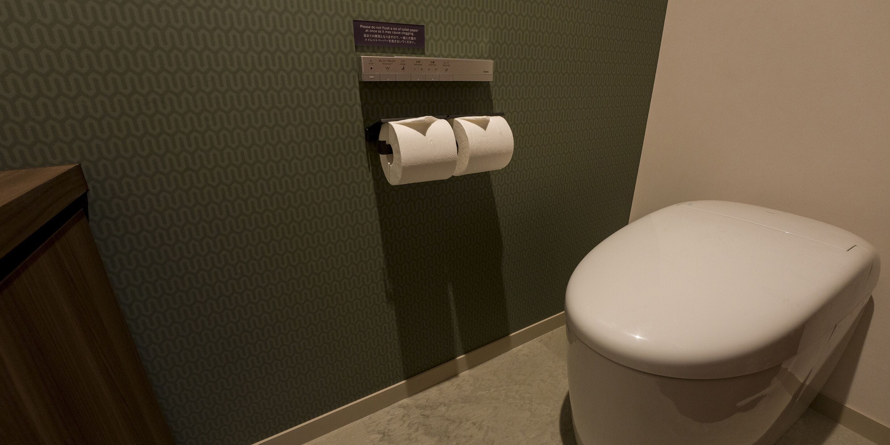 A bathroom with a toilet, a paper towel dispenser, and a patterned wall.