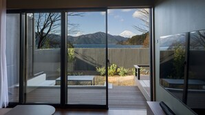 A modern room with a sliding glass door leading to an outdoor deck with a view of a mountain and a lake.