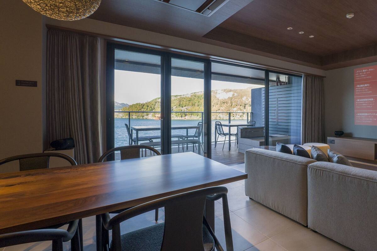 A modern living room with a large window, a wooden dining table, and a sofa.