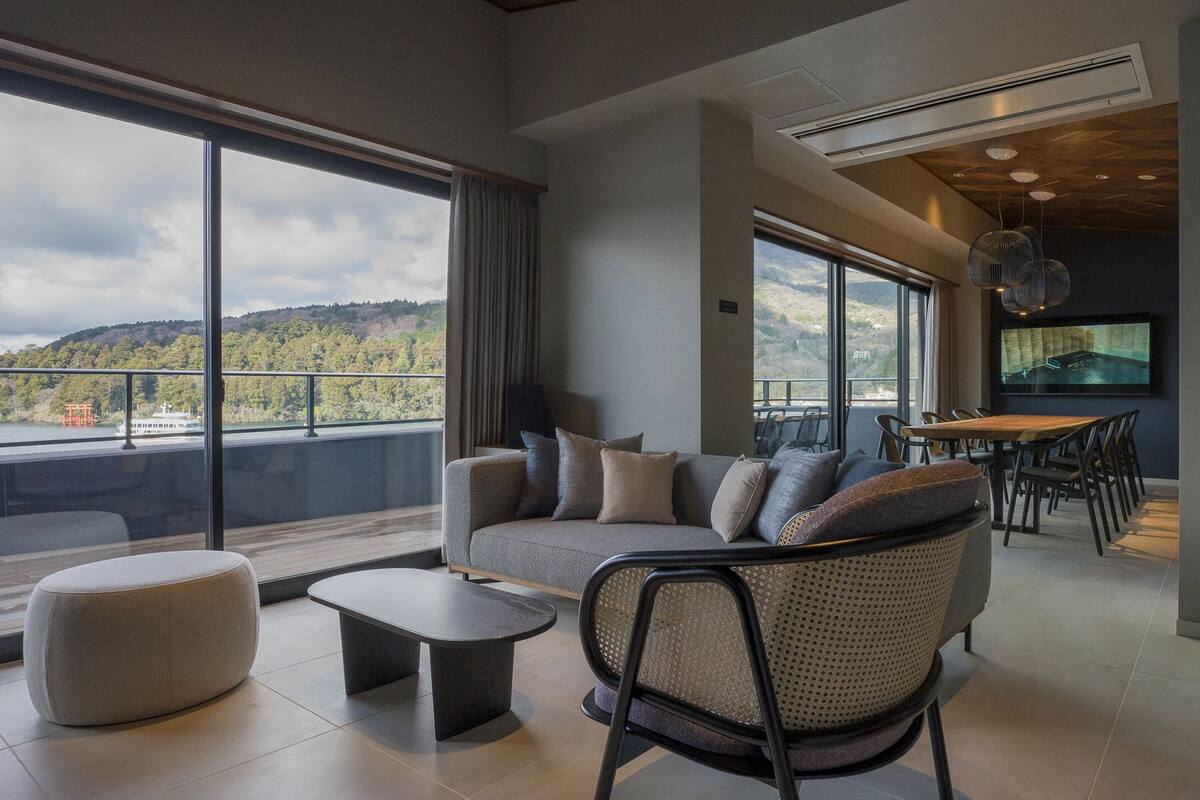 A modern living room with a large window, a sofa, a coffee table, and a dining area.