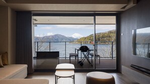 A modern living room with a sofa, a small table, and a view of a lake and mountains through a sliding glass door.