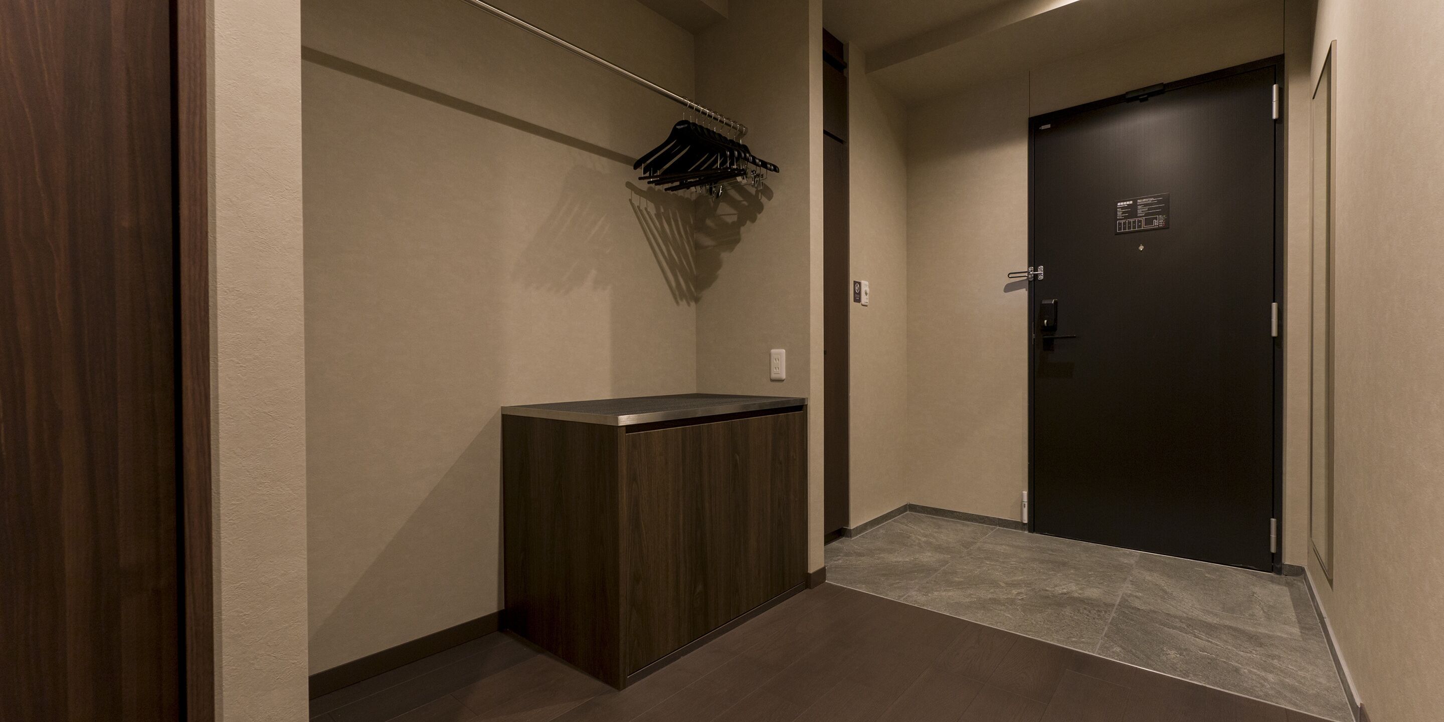 A hallway with a dark wooden cabinet, a coat rack with hanging items, and a dark door with a sign.