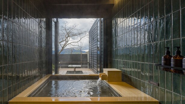 A modern spa with a hot tub, tiled walls, and a view of trees and mountains.