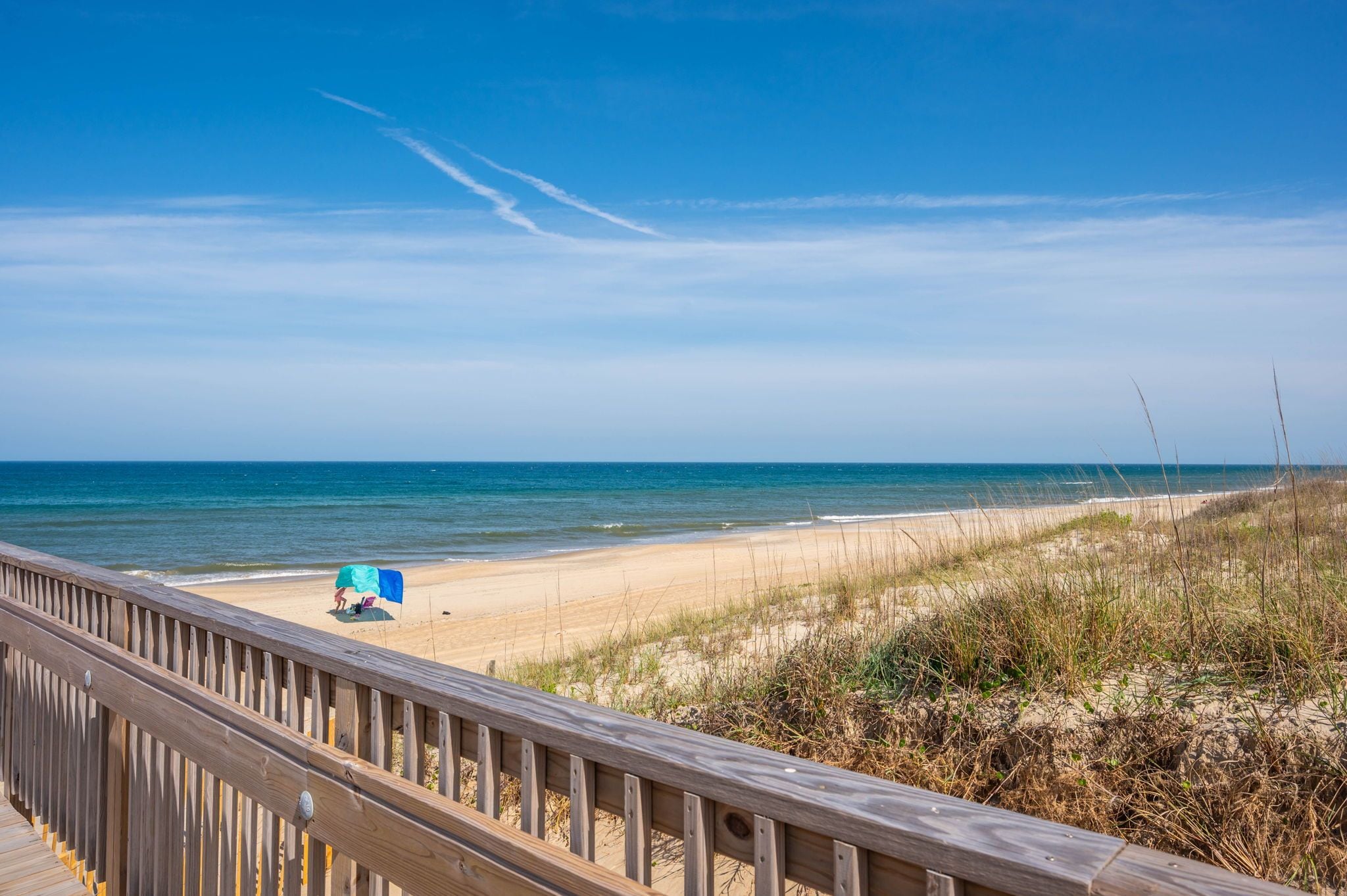 Ein Strand mit einer Holzpromenade, feinem Sand und einem klaren, blauen Himmel.
