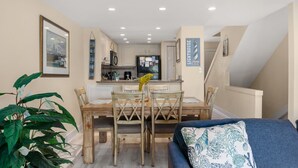 Una cocina compacta con armarios blancos, una mesa de comedor con sillas y una escalera que lleva a un nivel superior.