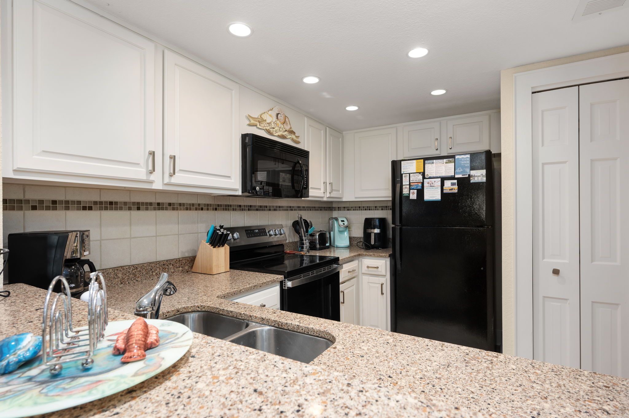 A kitchen with white cabinets, a black microwave, a black refrigerator, and a granite countertop.