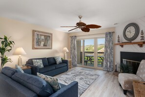 Un salon doté d’un ventilateur de plafond, d’une cheminée et d’une grande fenêtre donnant sur l’extérieur.