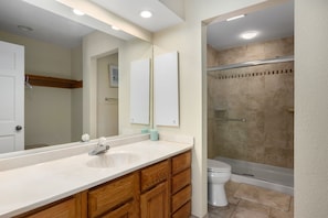 A bathroom with a large mirror, wooden vanity, white sink, and a glass-enclosed shower area.