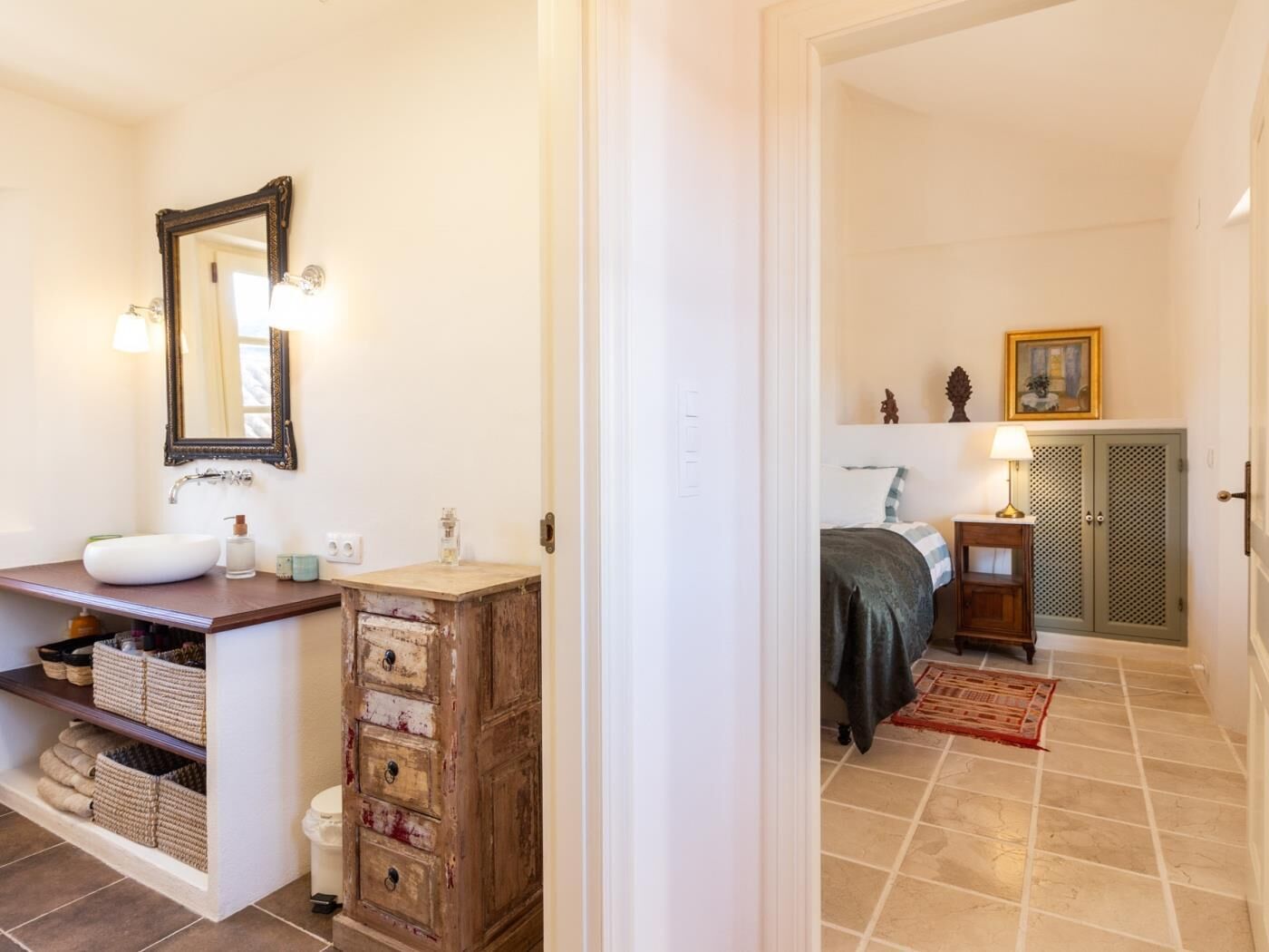 Un baño con lavamanos blanco, espejo y mueble de madera con cajones.
