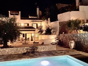 Une maison à deux étages avec une piscine, des murs en pierre et un espace salon extérieur.