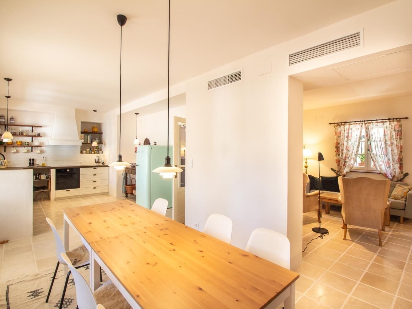 Une cuisine moderne avec des meubles blancs, une table à manger en bois et des luminaires suspendus.