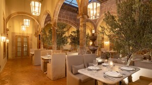 An indoor dining area with arched ceilings, stone walls, and olive trees. Tables are set with plates, glasses, and cutlery. - Casa Alondra (Morelia)