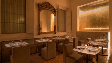 A restaurant with multiple tables set for dining, a large mirror, and a modern light fixture on the wall.