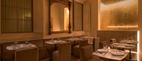 Un restaurante con varias mesas dispuestas para comer, un espejo grande y una lámpara moderna en la pared.