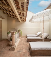 Ein sonnendurchfluteter Außenbereich mit zwei Liegestühlen, einer Pergola und Topfpflanzen.