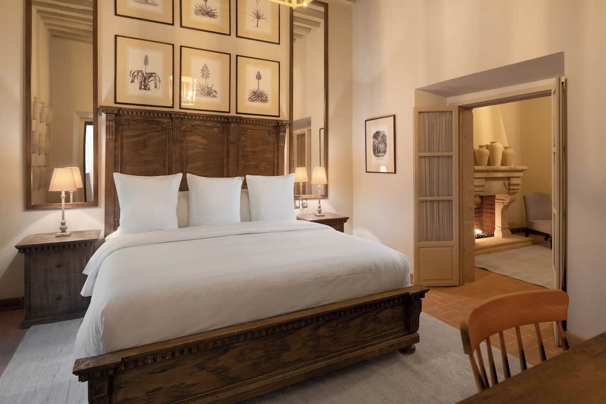 A bedroom with a large bed, wooden headboard, and framed botanical prints on the wall.