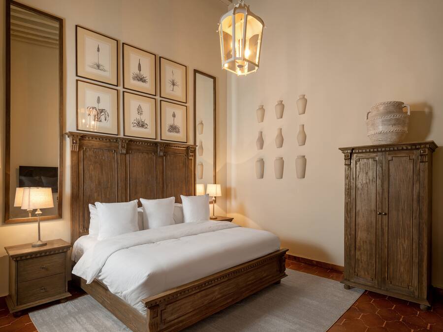 Une chambre à coucher avec un lit en bois, des tables de chevet avec des lampes, des reproductions botaniques encadrées accrochées au mur et une commode avec des vases.