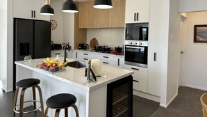 Une cuisine moderne avec des meubles blancs, un îlot central doté de tabourets, des suspensions noires et un four encastré.