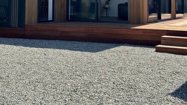 Une maison moderne avec une façade en bois, de grandes portes vitrées et une allée gravillonnée.