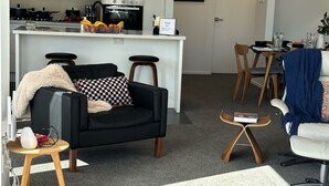 Un salon moderne avec un canapé noir, un fauteuil blanc et une table basse. Il y a également un coin cuisine avec une table à manger et des chaises.