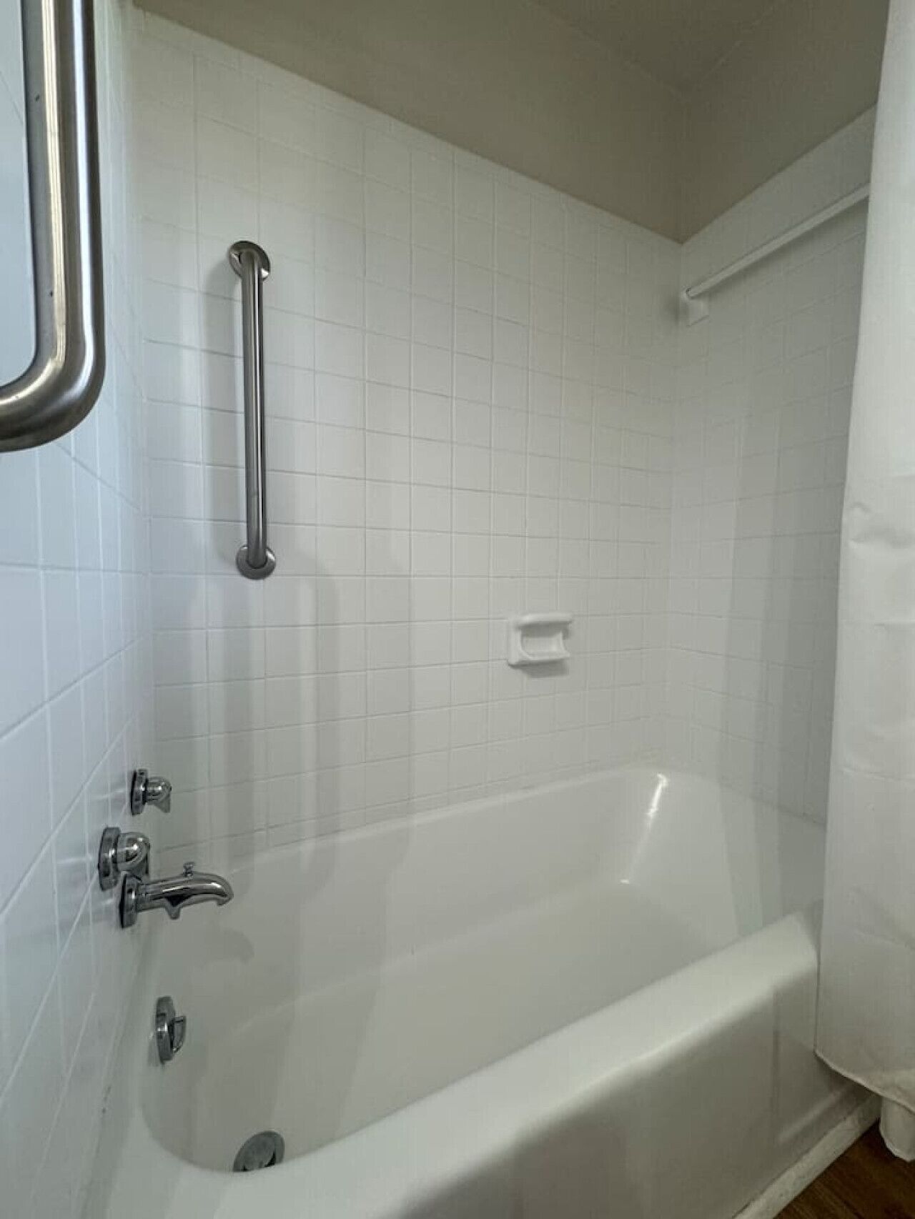 Een badkamer met een witte badkuip, een handgreep en een douchegordijn.