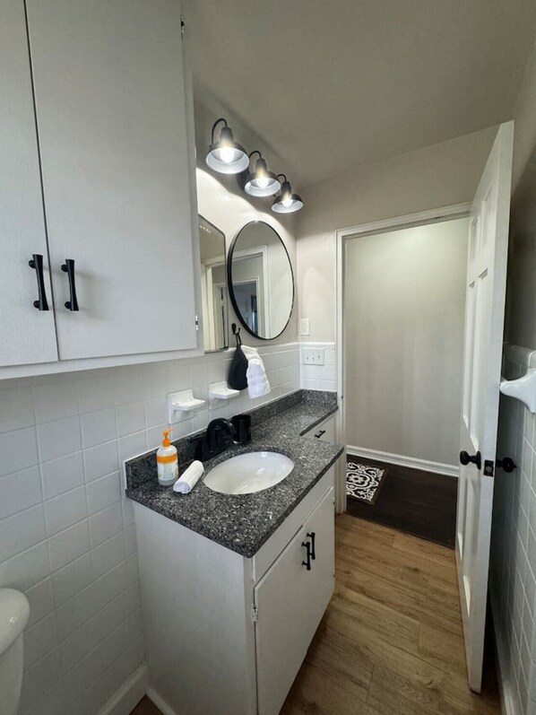 A modern bathroom with a white sink, black faucet, and a mirror above it. There are three lights above the mirror and a towel rack on the wall.