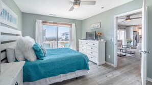 Een slaapkamer met een bed, een dressoir, een plafondventilator en een raam met gordijnen.