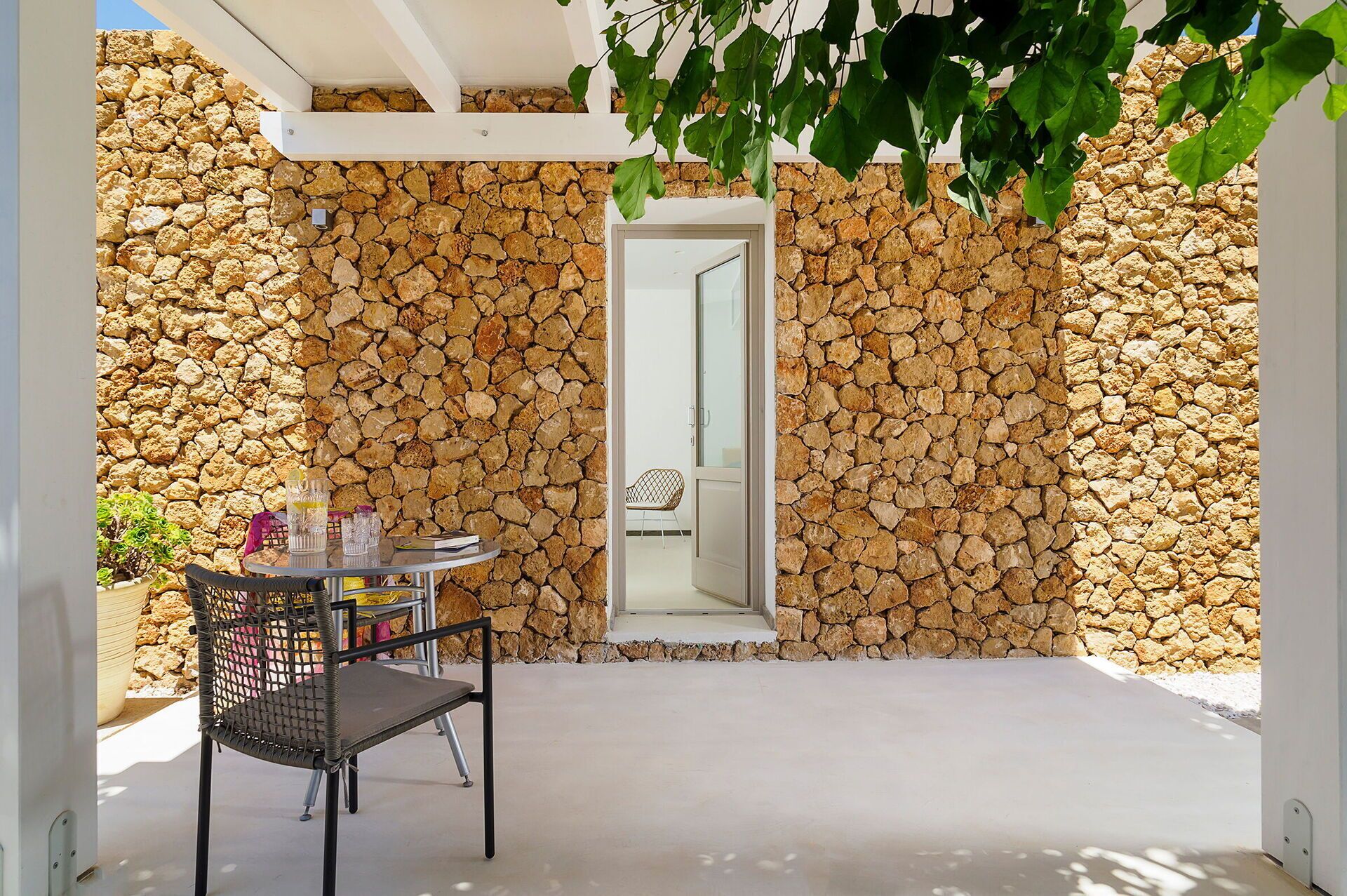 An outdoor seating area with a stone wall, a table with chairs, and a door leading to another room.