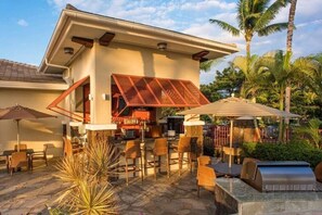 Relax in a stylish outdoor space with wicker furniture, a grill station, and lush greenery surrounding the modern building.