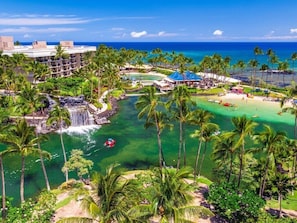 Een resort met zwembad, palmbomen, waterval en strand.