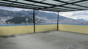 A concrete balcony with a metal roof, overlooking a mountainous town with buildings and a wind turbine. - Very private and quiet suite with a panoramic view of the entire city.  (Quito)