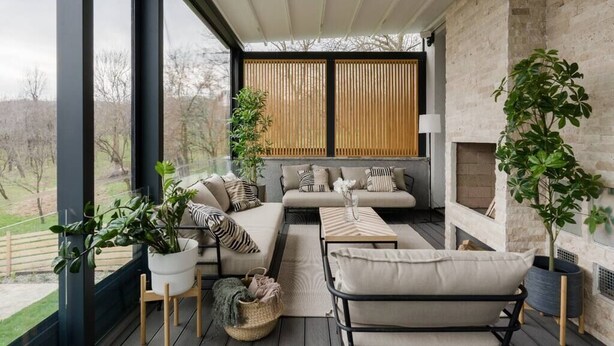 A modern living room with a sofa, armchairs, and a coffee table. There are potted plants and a fireplace.