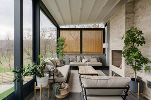 A modern living room with a sofa, armchairs, and a coffee table. There are potted plants and a fireplace. - Villa The Frame (Ghioșești)