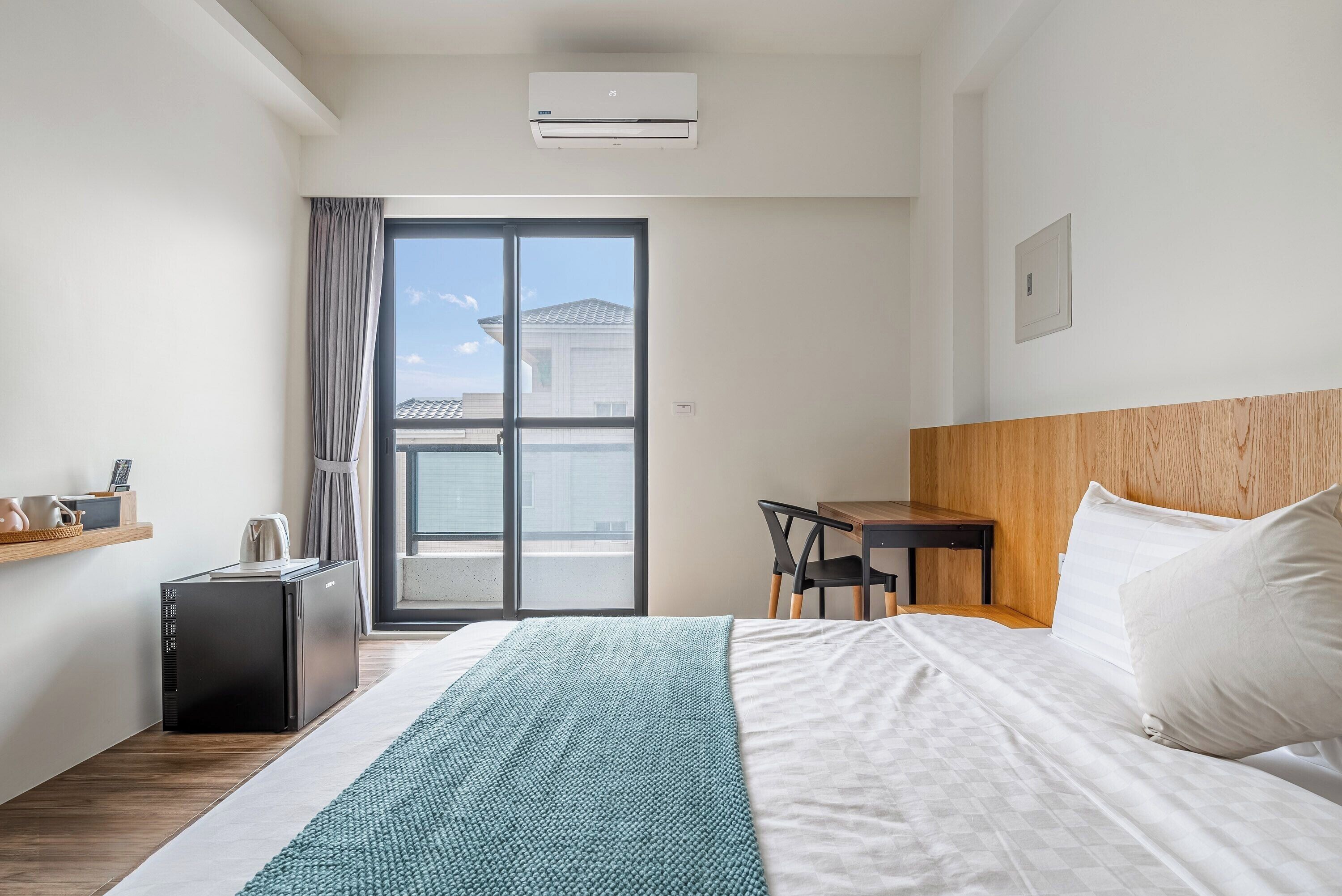 Ein Hotelzimmer mit einem Bett, einem Schreibtisch, einem Stuhl, einem kleinen Tisch, einem Wasserkocher und einem Fenster mit Vorhängen.