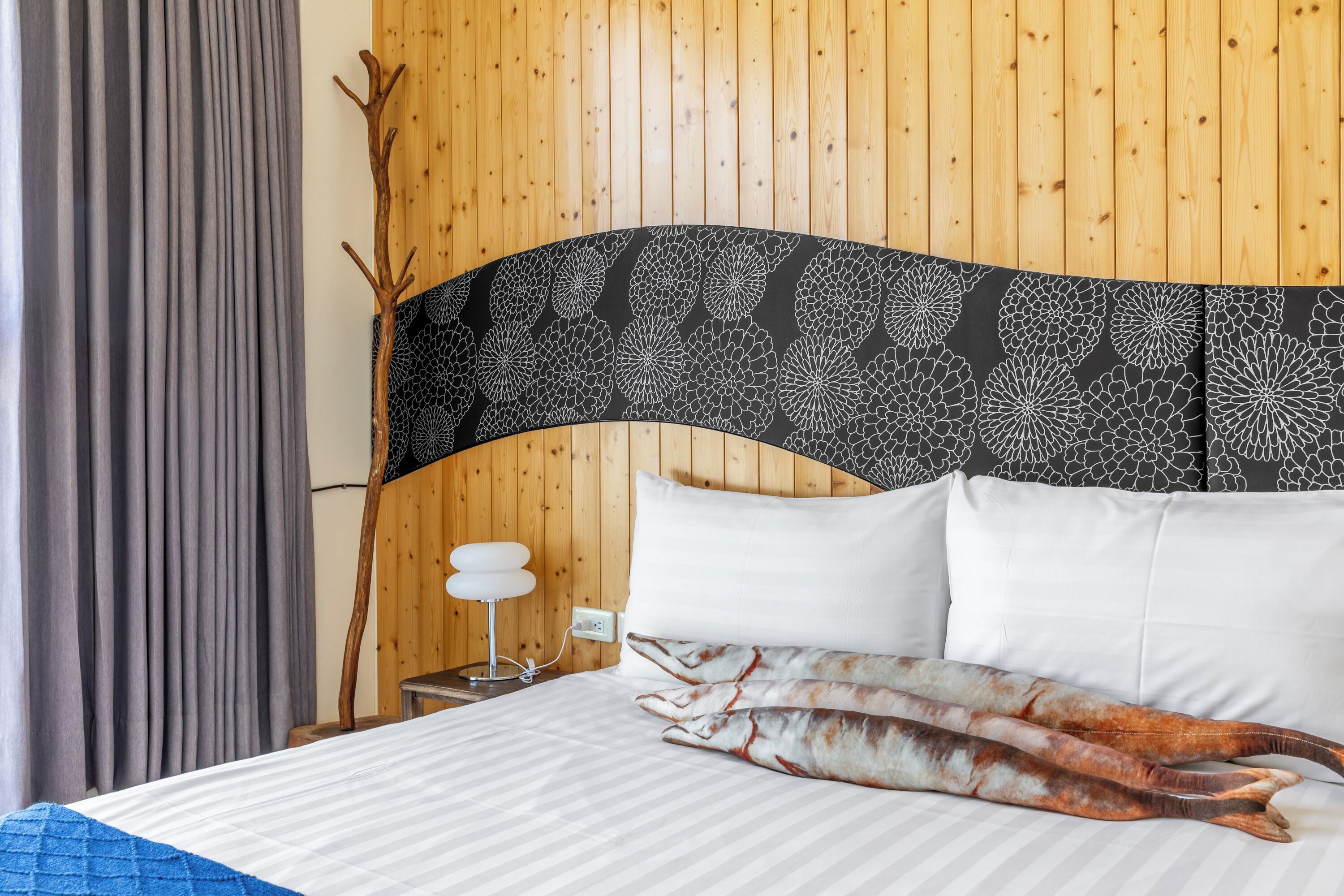 A hotel room with a wooden paneled wall, a bed with white bedding, a decorative headboard, and a nightstand with a lamp.