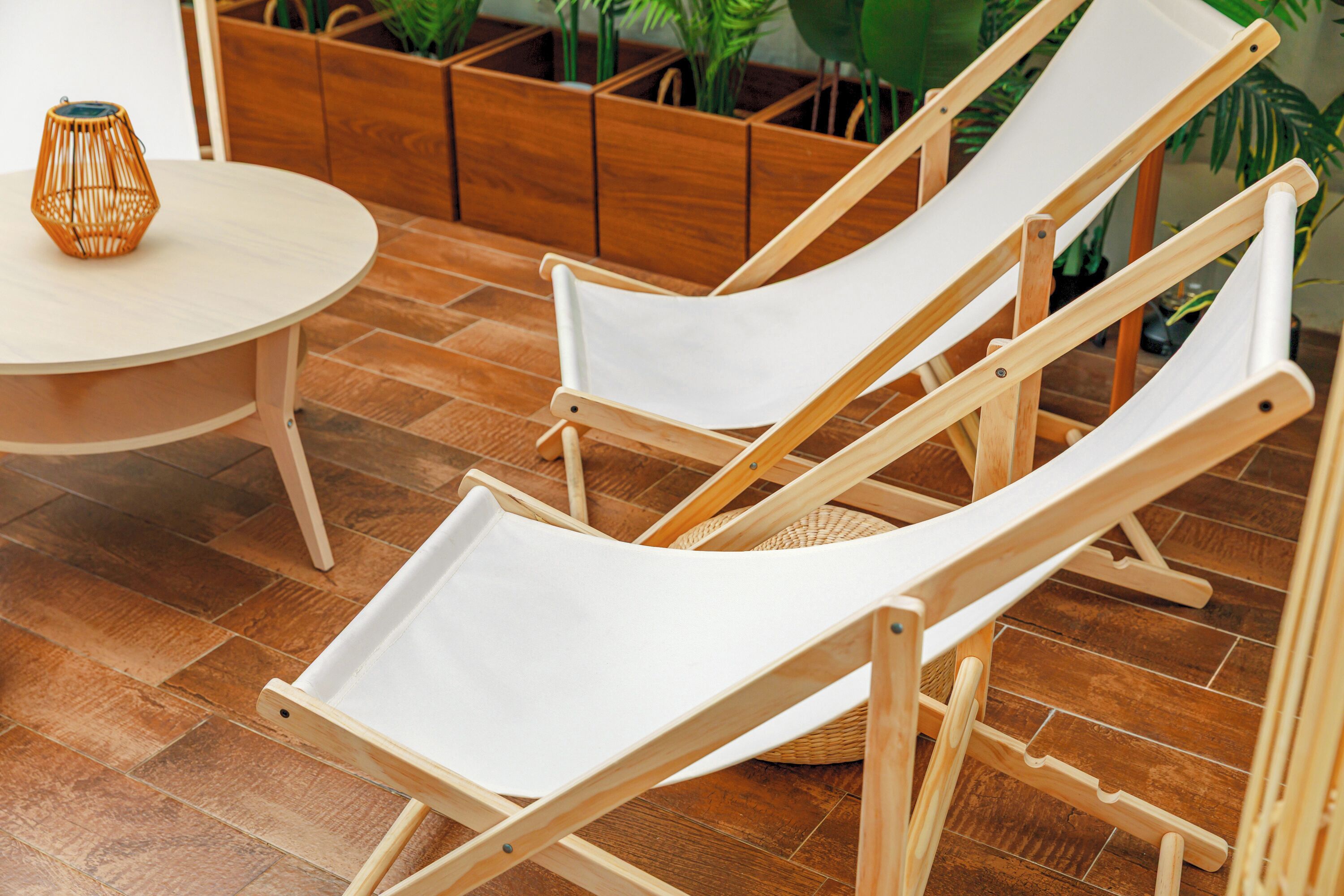 Two wooden lounge chairs with white canvas seats, a round wooden table, and a woven basket on a wooden floor.