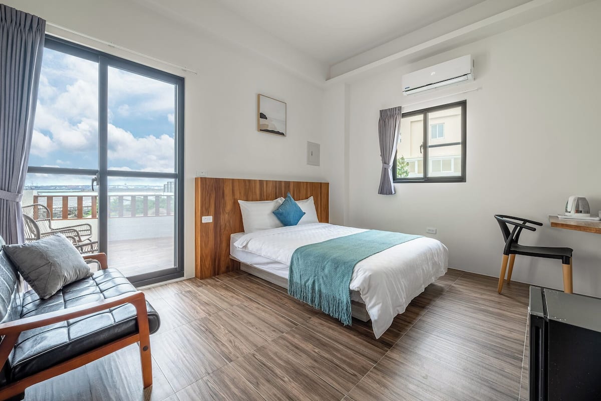 A hotel room with a bed, a chair, a desk, and a view of the outside.