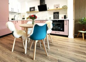 A modern kitchen with wooden flooring, a round table, and two chairs with fluffy white and blue upholstery. - RoseWood Boutique Apartment - In Green Future Spa (Sinaia)