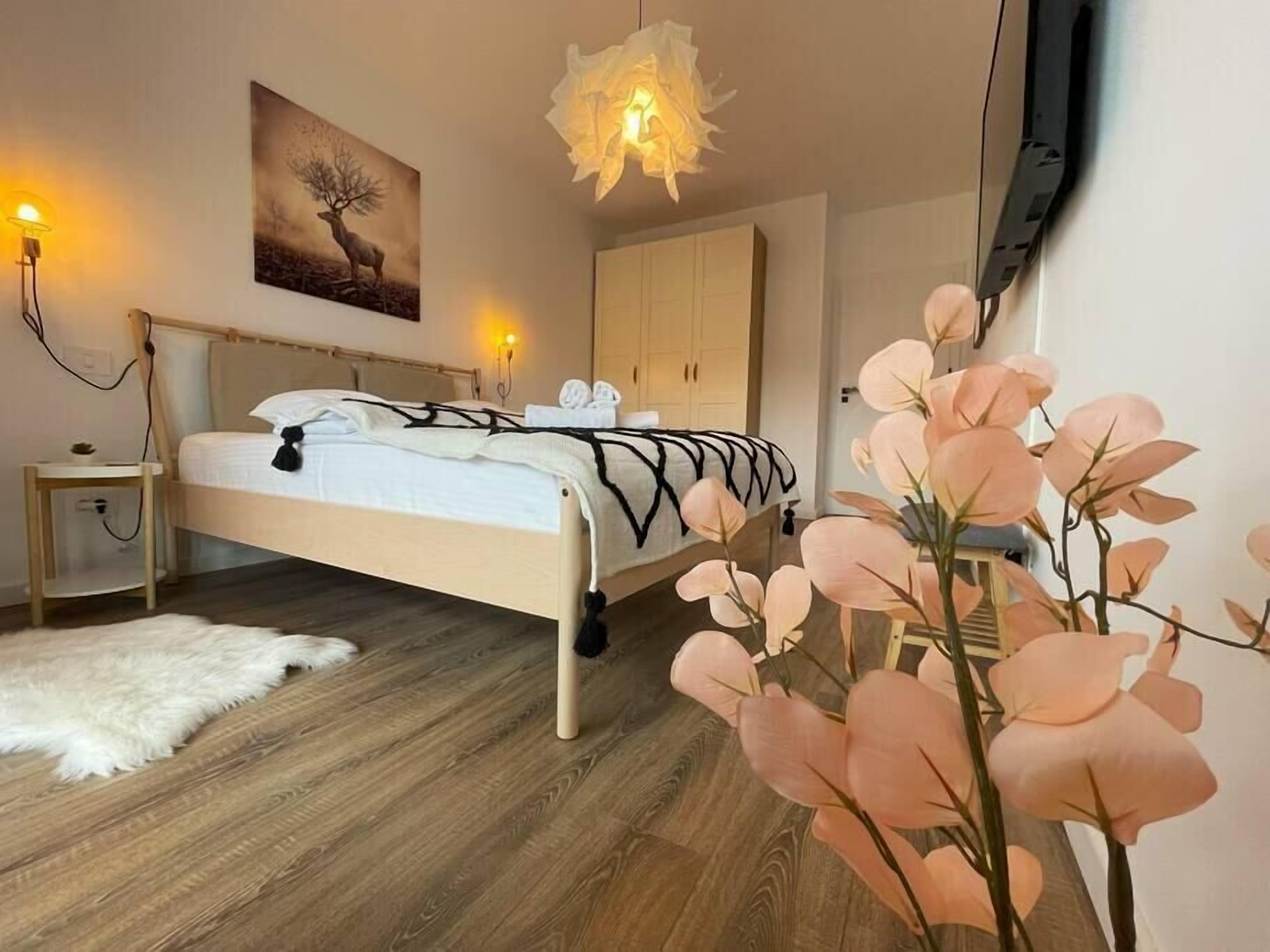 A bedroom with a bed, bedside lamps, a painting, a wardrobe, and a white rug.