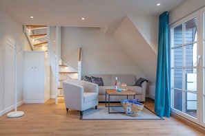 Un moderno loft con soffitto alto, una scala, un divano, un tavolino da caffè e un'ampia finestra con tende.